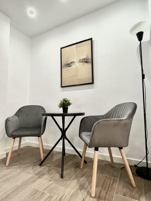 Zona de estar moderna en apartamento de Valencia con dos sillas tapizadas grises, mesa redonda negra y planta en maceta