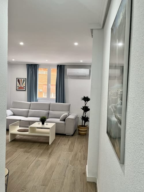 Sala de estar moderna de un apartamento en Valencia con sofá gris, mesa de café blanca y vistas a la ciudad