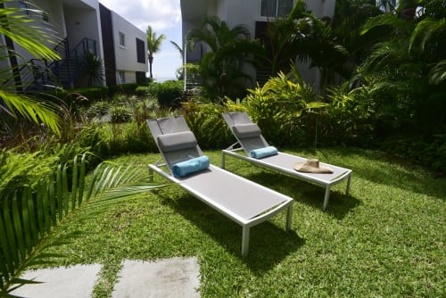 Two lounge chairs with blue cushions on lush green lawn surrounded by tropical palm plants at Unik Properties,