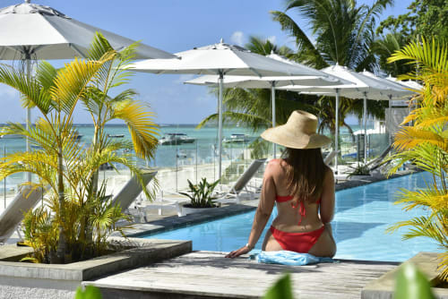 Woman in red swimsuit and hat relaxing by pool at Unik Properties apartment in Trou-aux-Biches, Mauritius, with ocean view