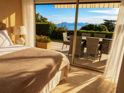 Chambre de luxe à Cannes avec terrasse vue mer, fauteuils en rotin et paysage méditerranéen de l'appartement LE SAINT GEORGES.