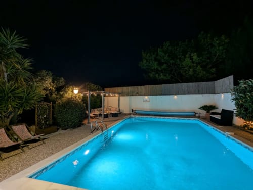 Piscine privée illuminée de nuit avec chaises longues, murs blancs et plantes tropicales au gîte La Closerie à La Redorte