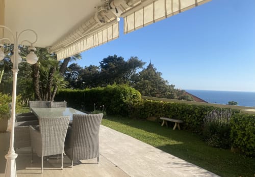 Shaded terrace with wicker chairs overlooking Mediterranean Sea and lush garden at Cannes luxury apartment