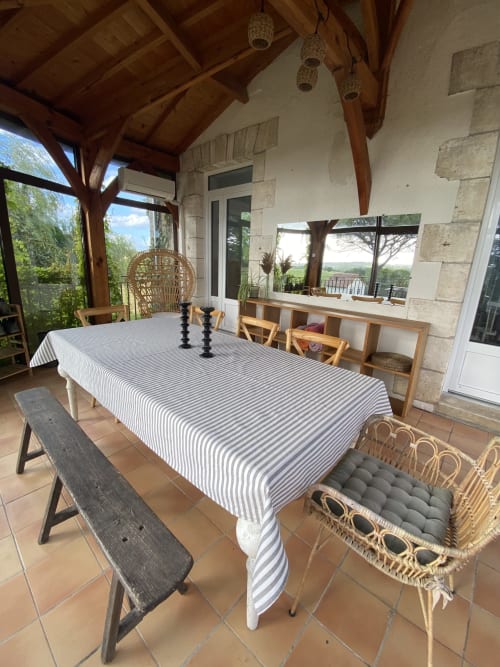 Patio couvert du gîte Le Domaine les Olivoux à Pomport avec nappe rayée, chaises en rotin et vue campagnarde