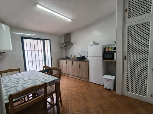 Luminosa sala de estar-comedor en la villa Las Mellis, Antequera, con mesa de madera, electrodomésticos modernos y suelo de baldosa de barro.