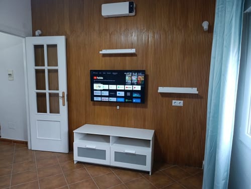 Sala moderna con televisor de pantalla plana, consola blanca, paredes con textura de madera, aire acondicionado y diseño contemporáneo