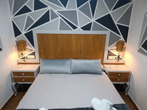 Dormitorio moderno con almohadas azules, cabecero de madera, lámparas gemelas y arte geométrico en villa Las Mellis, Antequera
