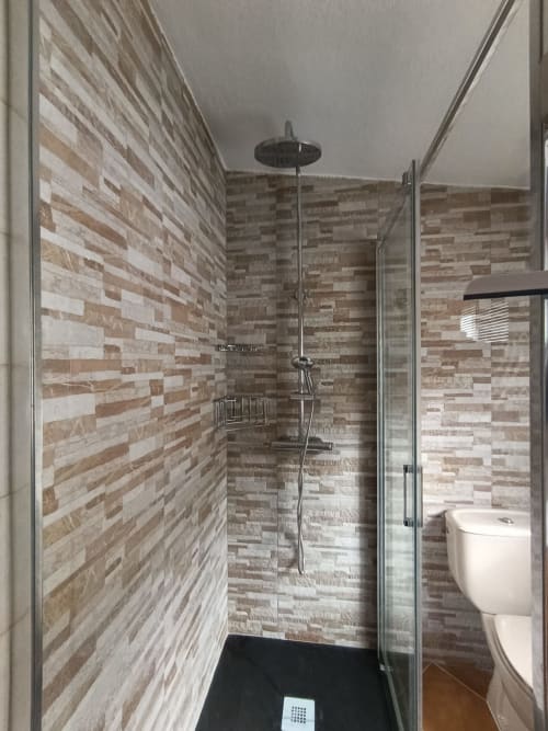 Moderno baño con ducha abierta, azulejos de ladrillo beige, alcachofa de lluvia y mamparas de vidrio en la villa Las Mellis de Antequera