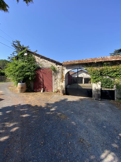 Entrée de maison en pierre au Domaine les Olivoux à Pomport avec porte rouge, portail noir et murs couverts de lierre sous ciel dégagé