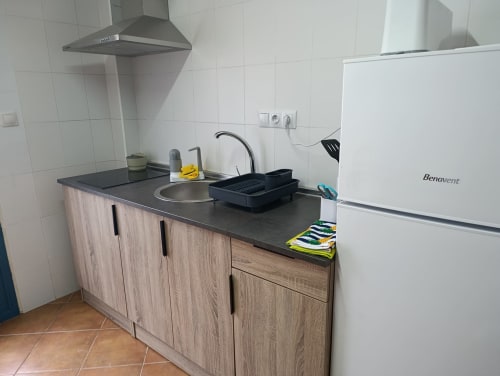 Área de cocina moderna con muebles de madera, encimera negra, fregadero, estufa y refrigerador Benavent blanco en villa Las Mellis.