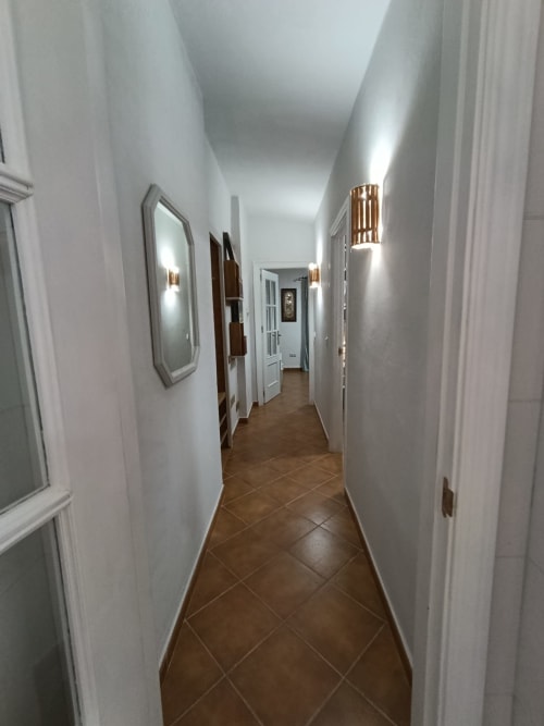Pasillo moderno en villa Las Mellis, Antequera con paredes blancas, suelos de baldosa marrón, espejos e iluminación ambiental