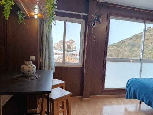 Habitación de villa moderna en Antequera con vistas a la montaña, paneles de madera oscura, mesa de comedor y ropa de cama azul con vista al casco histórico