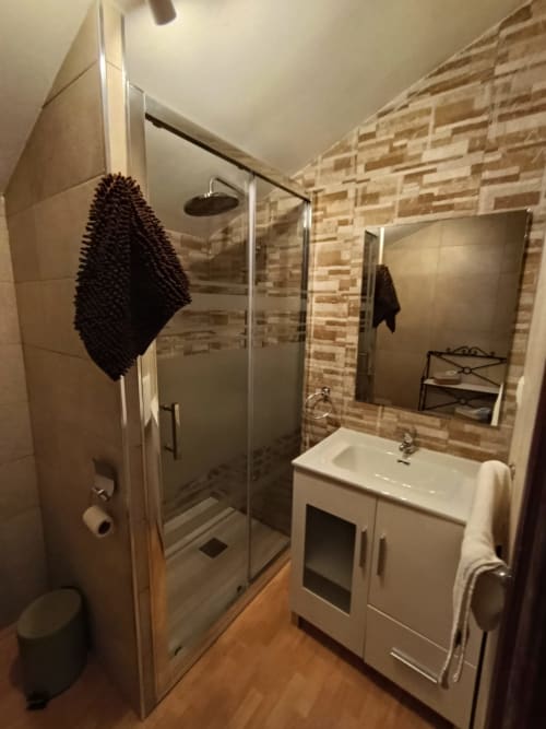 Baño moderno con ducha tipo walk-in, tocador blanco y pared con azulejos decorativos en la villa Luna de Antequera