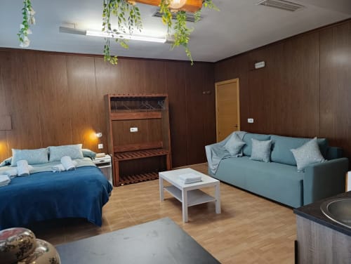 Dormitorio espacioso con cama azul, sofá turquesa, paredes de madera y plantas colgantes en Luna villa, Antequera