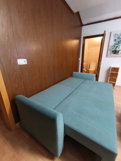 Sofá cama azul claro en el dormitorio de la villa Luna de Alojamientos Las Mellis, Antequera, con paredes de madera y puerta abierta