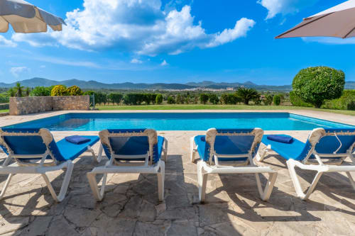 Lujosa zona de descanso junto a la piscina de villa Massa Properties en Artá con vistas montañosas, tumbonas azules y sombrillas