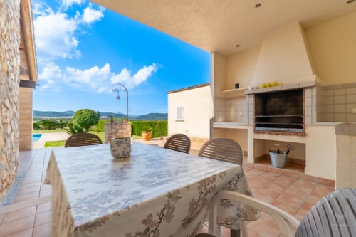 Terraza cubierta de la villa Can Terres en Artá con mesa de comedor, barbacoa integrada, vistas a las montañas y piscina