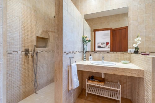Baño moderno en villa Can Terres, Artá, con ducha a ras de suelo, tocador de madera, espejo grande y paredes con azulejos beige