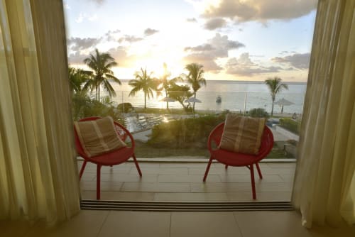 Beachfront balcony with red chairs overlooking palm trees and ocean sunset at Cap Ouest apartment, Flic en Flac, Mauritius