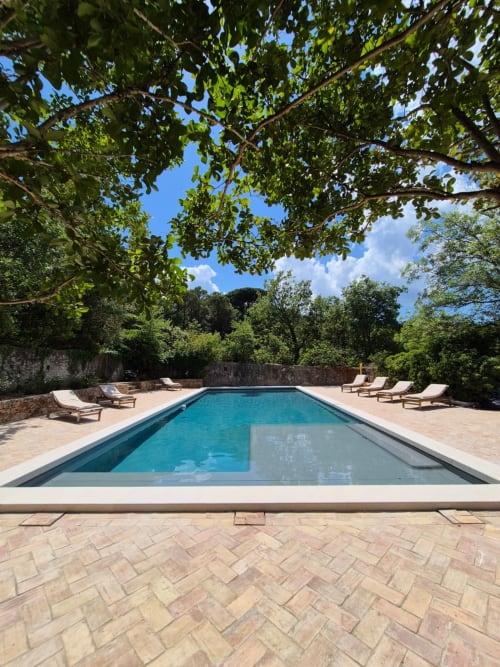 Piscine rectangulaire avec chaises longues à la Ferme Saint-Georges en Provence, entourée de verdure luxuriante et de murs en pierre