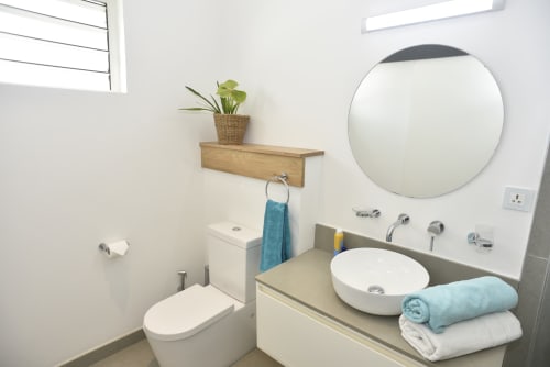 Modern bathroom in O'Biches apartment featuring round mirror, white vessel sink, toilet, and blue towels on vanity counter
