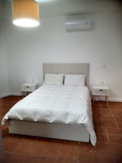 Quarto moderno na pousada Casa Augusta em Braga com cama queen, roupa de cama branca, cabeceira bege, mesinhas de cabeceira, luminária pendente