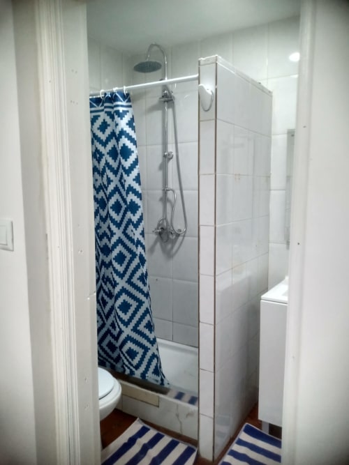 Banheiro moderno com chuveiro de vidro, toalha geométrica azul e branca, e azulejos metro brancos na Casa Augusta