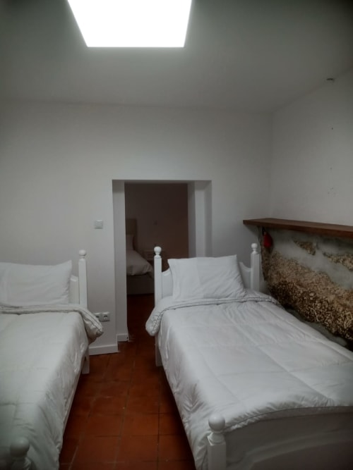 Quarto duplo da Casa Augusta hostel em Braga, Portugal, com roupa de cama branca, piso de madeira, claraboia e banheiro privativo