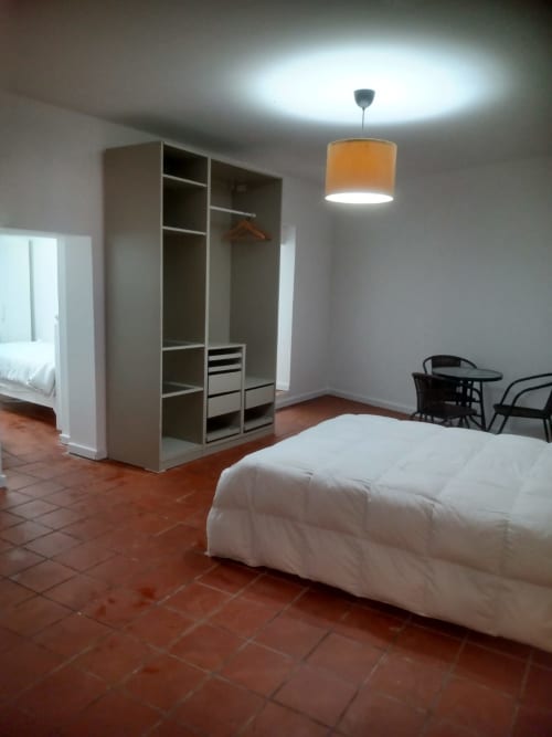 Quarto espaçoso da pousada Casa Augusta em Braga com cama branca, guarda-roupa, luminária pendente e piso de barro