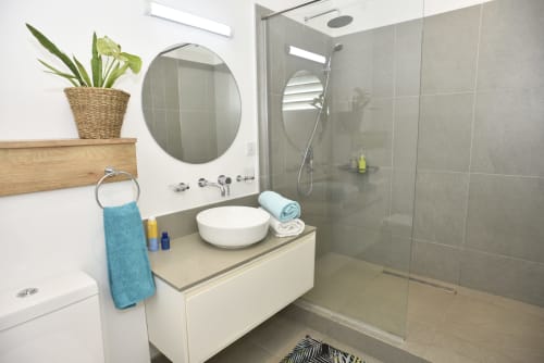 Modern bathroom at O'Biches Premium Apartment in Trou-aux-Biches with circular mirror, vessel sink, glass shower, and plant