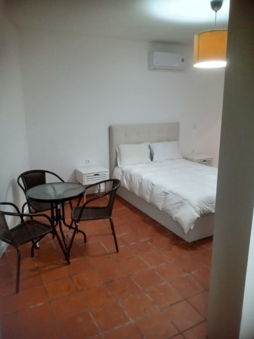 Quarto C5 da pousada Casa Augusta com cama, roupa branca, criado, cadeiras pretas, mesa redonda, piso em terracota e ar condicionado