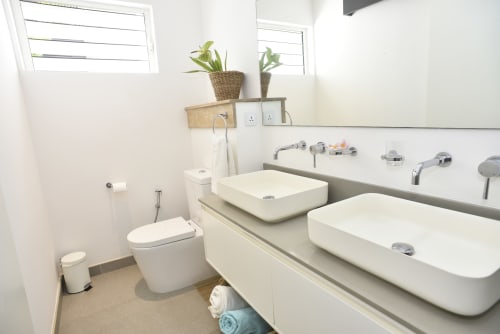 Modern bathroom in O'Biches Premium Holiday Apartment with dual vessel sinks, toilet, mirror, and potted plants at