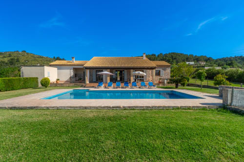 Villa de lujo en Artà con piscina, tumbonas azules y jardines cuidados bajo cielo despejado