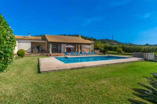 Villa de lujo en Artà con piscina, tumbonas azules y jardines impecables bajo cielo despejado