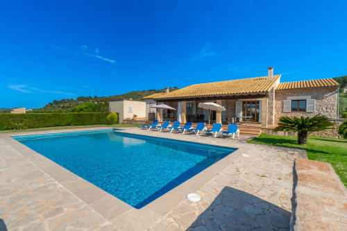 Villa de lujo en Artà con piscina azul reluciente, tumbonas, terraza de barro cocido y arquitectura de piedra bajo cielo despejado