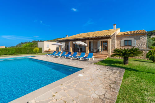 Villa de lujo en Artà con piscina azul, tumbonas, casa de piedra y jardines cuidados bajo cielo despejado