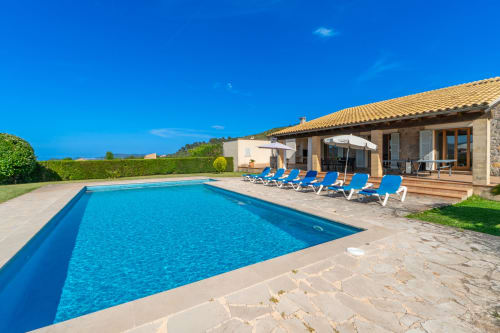 Villa de lujo en Artà con piscina rectangular, tumbonas azules y terraza de piedra bajo cielo despejado