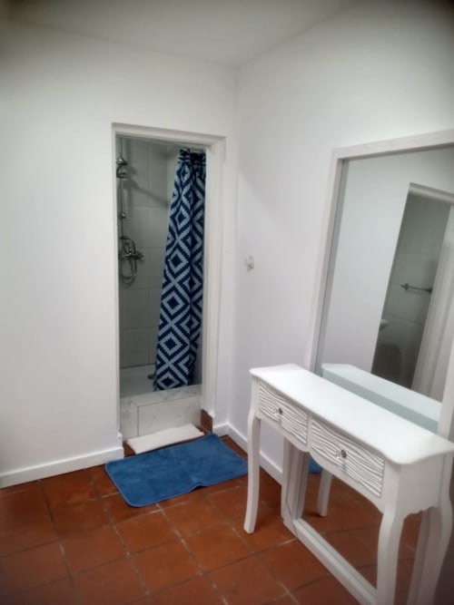 Banheiro da casa de hóspedes Casa Augusta em Braga com chuveiro, tapete azul, pia branca e espelho no quarto C5 Mariquinha