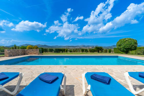 Piscina de lujo en Massa Properties en Artà con tumbonas azules, vistas a la montaña y cielo despejado