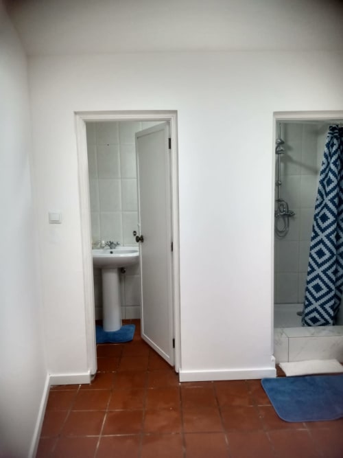 Corredor da casa de banho da pousada Casa Augusta em Braga com lavatório, chuveiro com toalha azul e piso em azulejos de barro