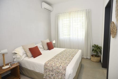 Bright bedroom with white bed, red pillows, air conditioning unit, sheer curtains, and potted plant at O'Biches Premium