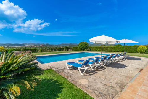 Piscina de lujo con tumbonas azules y sombrilla en Massa Properties, Artà, España, con vistas a las montañas