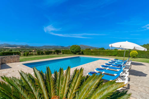 Piscina del resort con tumbonas azules, sombrilla blanca y vistas a las montañas en Artà, Mallorca