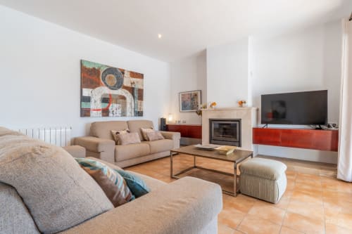 Moderno salón en Artà con sofás beige, chimenea, TV de pantalla plana y obra de arte abstracto