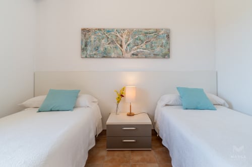 Dormitorio doble con almohadas turquesas, mesita de noche compartida y cuadro de árbol en Massa Properties, Artà