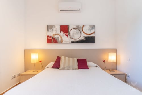 Moderno dormitorio en Massa Properties de Artà con cama blanca, almohadas burdeos, lámparas de noche y obra de arte abstracta