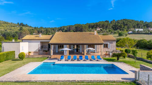 Villa de lujo en Artà con piscina, tumbonas y arquitectura de piedra rodeada de jardines exuberantes