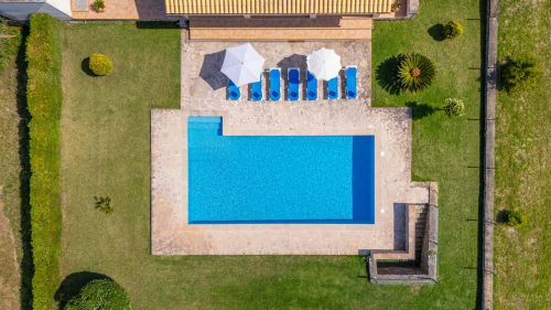 Vista aérea de la piscina de Massa Properties en Artà con tumbonas azules, sombrillas y jardines circundantes