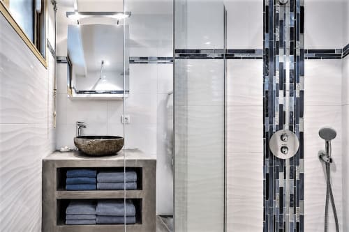 Modern bathroom in Cannes apartment with stone sink, glass shower, black and white tile accents, and towel storage shelving.