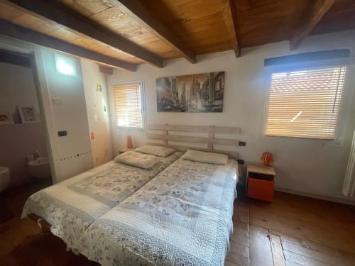 Camera luminosa della Casa Carmelo BnB a Schio con letto matrimoniale, travi in legno e ampie finestre con persiane